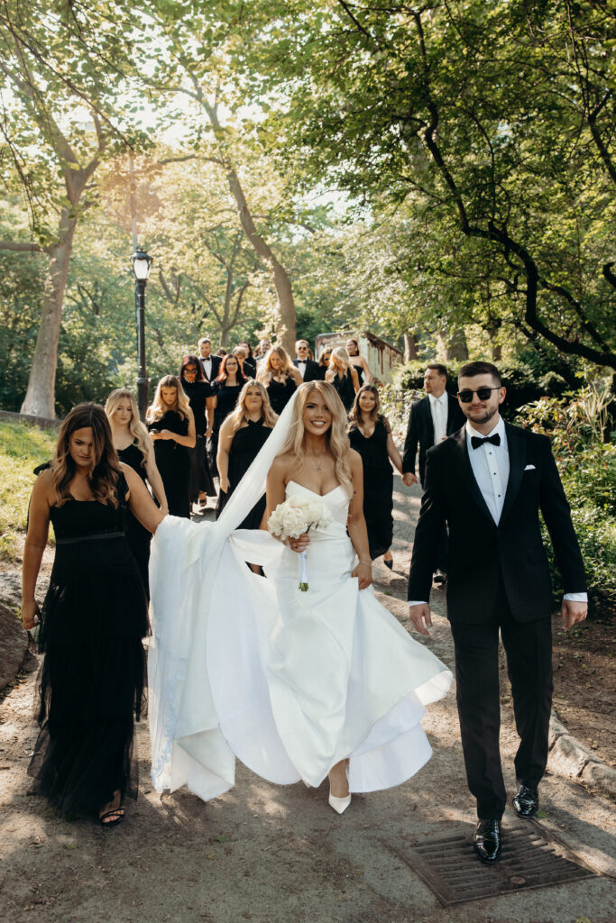 Bridesmaids and groomsmen help bride walk down the steps in Central Park