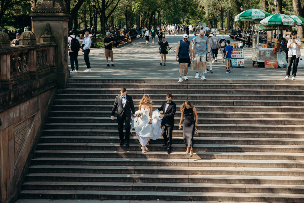 Bridesmaid and groomsmen help bride walk down the stairs