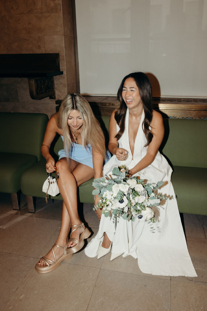 NYC bride and guest sitting on a chair while waiting for their elopement ceremony at NYC City Hall