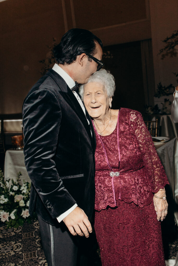 Groom kissing grandmother on the head at Le Chateau New York during wedding reception