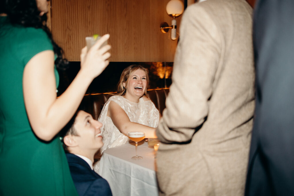 Bride laughing with guests while holding a cocktail during wedding reception