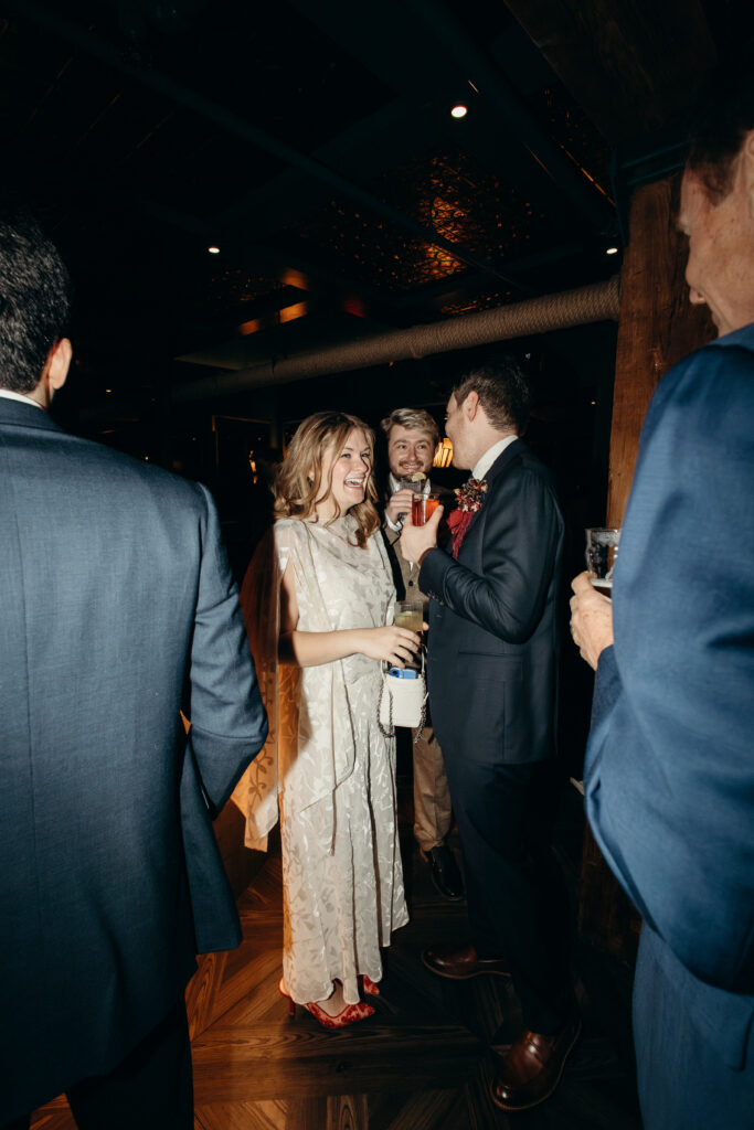 Bride smiling while talking with guests and holding cocktail at reception