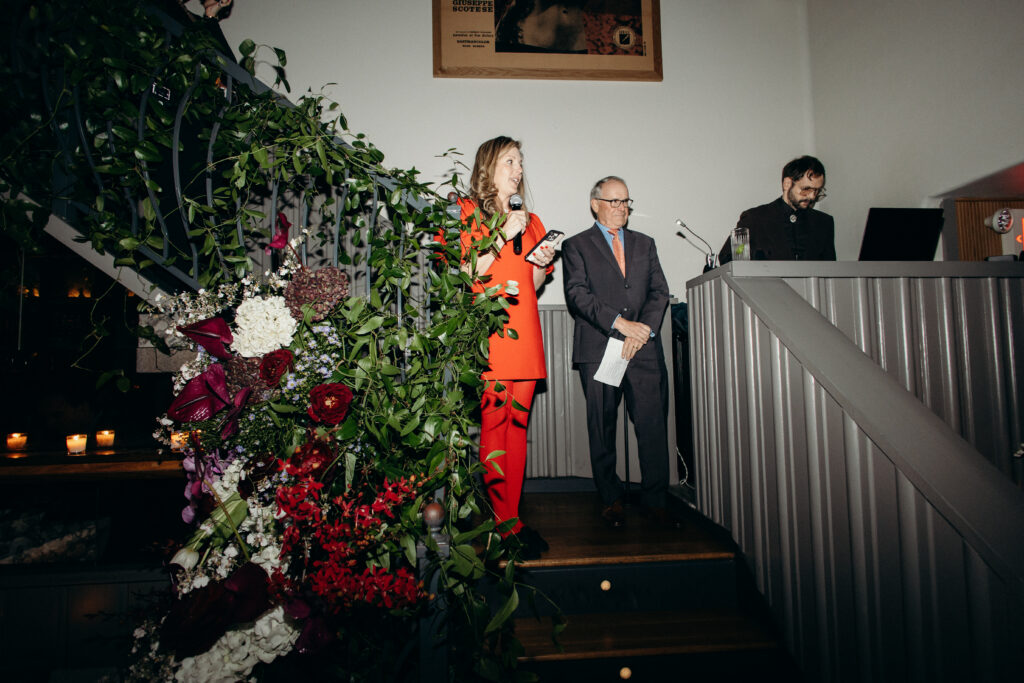 Wedding speech moment with speaker holding microphone beside floral installation