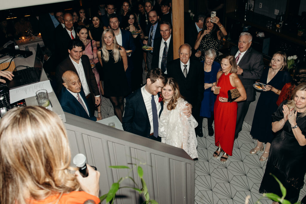 Couple surrounded by friends and family during reception toast moment