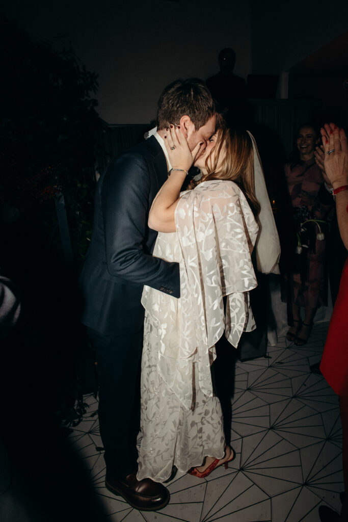 Bride and groom sharing first kiss during ceremony at Madeline’s Brooklyn