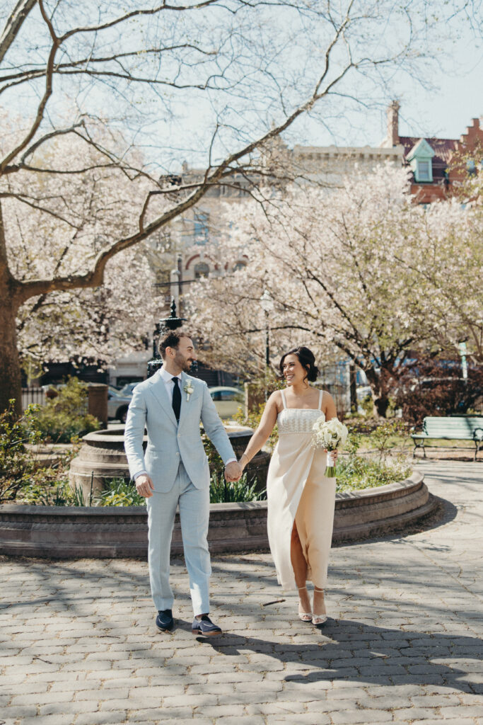 Newlywed couple walking hand in hand through a park filled with blooming spring trees