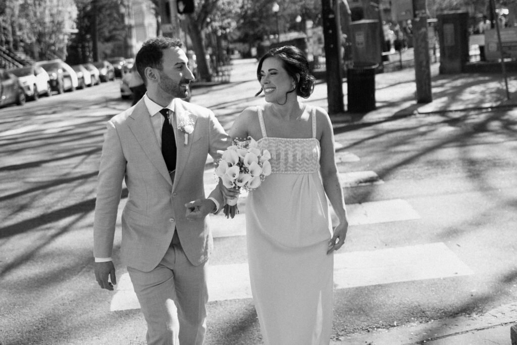 Black and white portrait of bride and groom walking arm in arm and smiling outdoors
