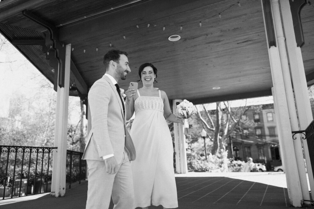 Bride and groom laughing together under a gazebo during their intimate park wedding ceremony