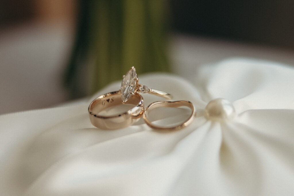 Close-up of gold wedding rings resting on a white satin ring pillow with soft natural light