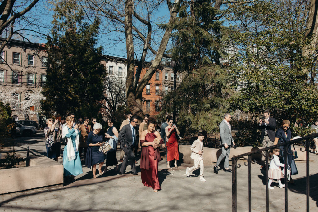 Wedding guests gathering for an intimate outdoor ceremony in a Jersey City park with blooming trees