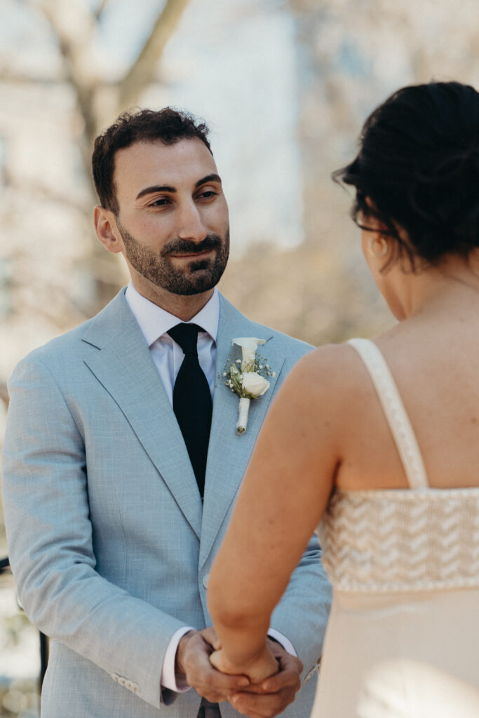 Close-up detail of the groom holding the bride’s hands during the ceremony