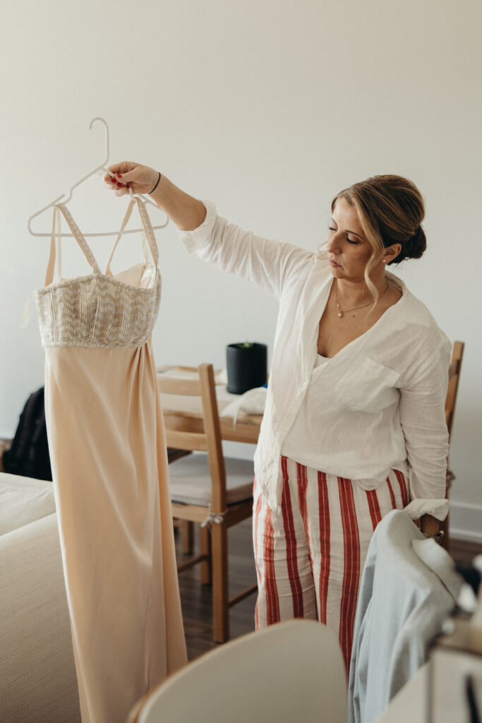 Woman holding up a light champagne-colored wedding dress while getting ready for the ceremony