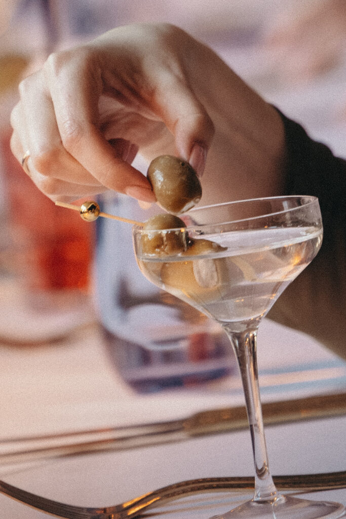Close-up of a martini glass garnished with green olives during the wedding reception cocktail hour