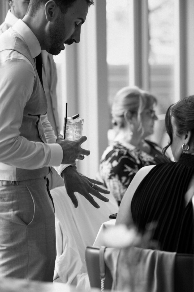 Groom holding a cocktail while talking with guests during the wedding reception in black and white