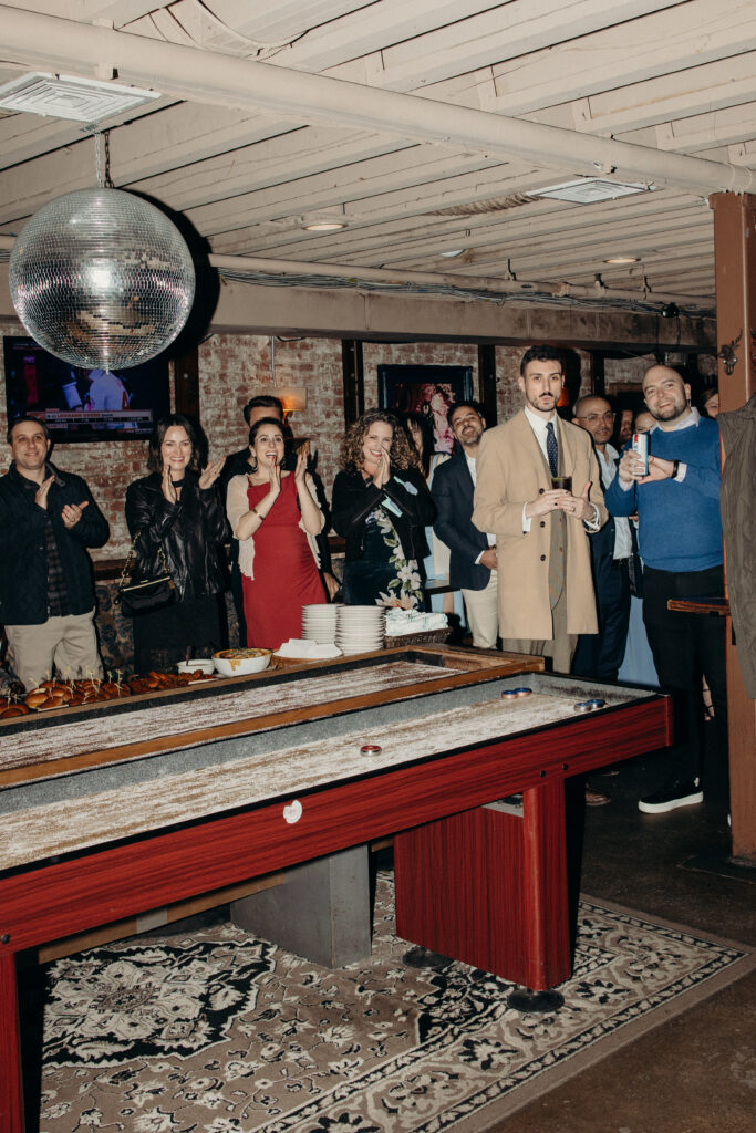 Guests gathered around a shuffleboard table cheering during Sean and Giana’s Jersey City elopement reception