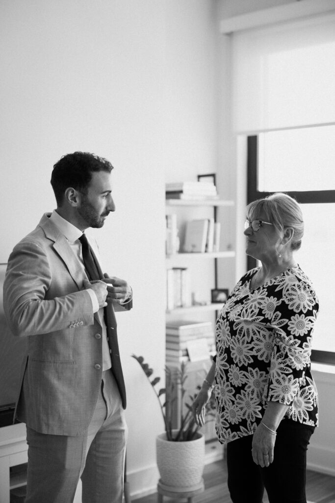 Groom fixing his tie while sharing a quiet moment with a family member before the ceremony