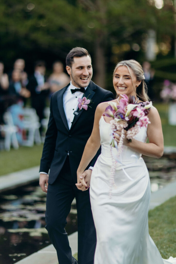 Newlyweds smiling as they walk hand in hand after the ceremony