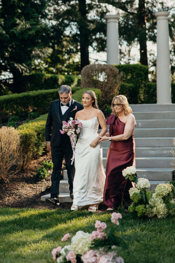 Bride walks with her parents toward the ceremony at The Ashford Estate