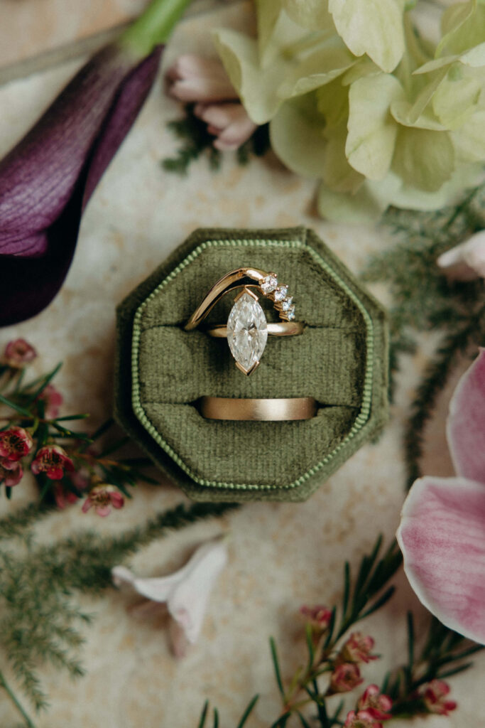 Marquise diamond engagement ring and gold wedding band displayed in a green velvet ring box