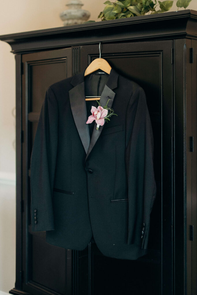 Groom's black tuxedo with a pink orchid boutonniere hanging before getting ready at The Ashford Estate