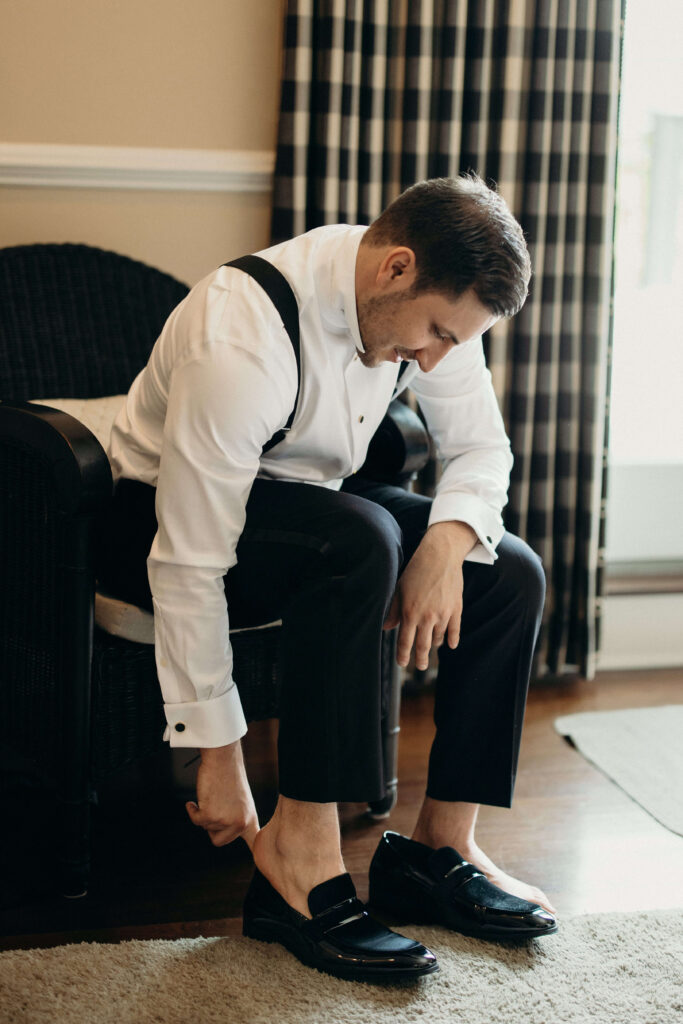 Groom putting on black dress shoes while getting ready for his wedding at The Ashford Estate