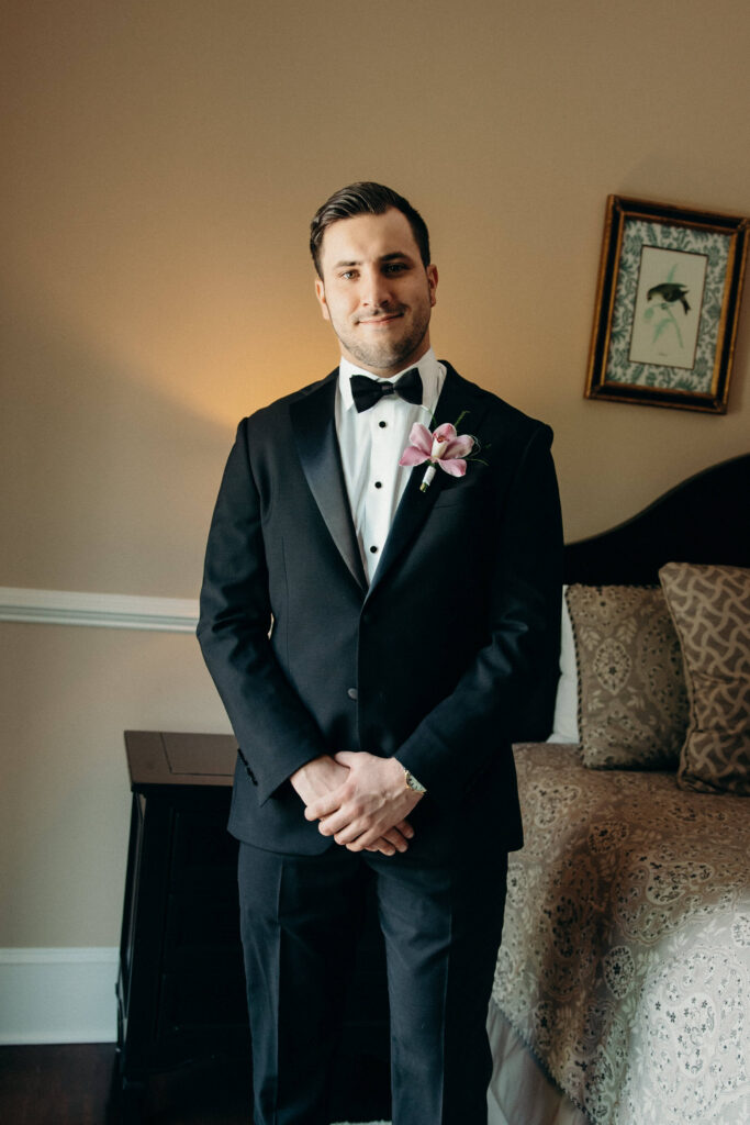 Groom portrait in a black tuxedo with a pink orchid boutonniere at The Ashford Estate