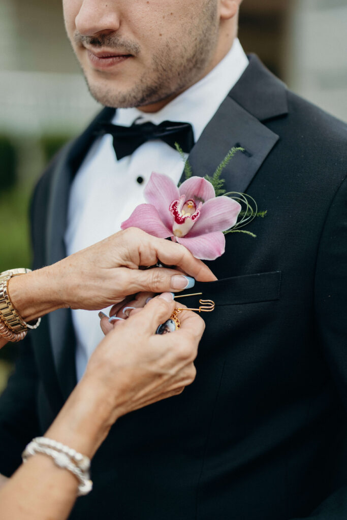 A family member pins the groom's orchid boutonniere onto his black tuxedo