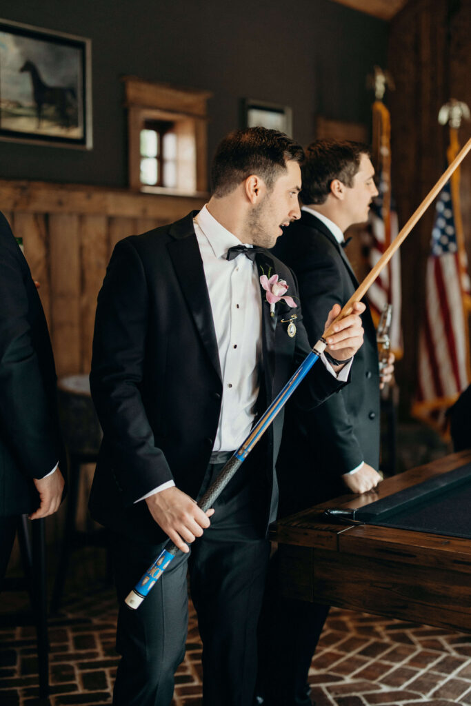 Groom holding a pool cue while spending time with his groomsmen before the ceremony