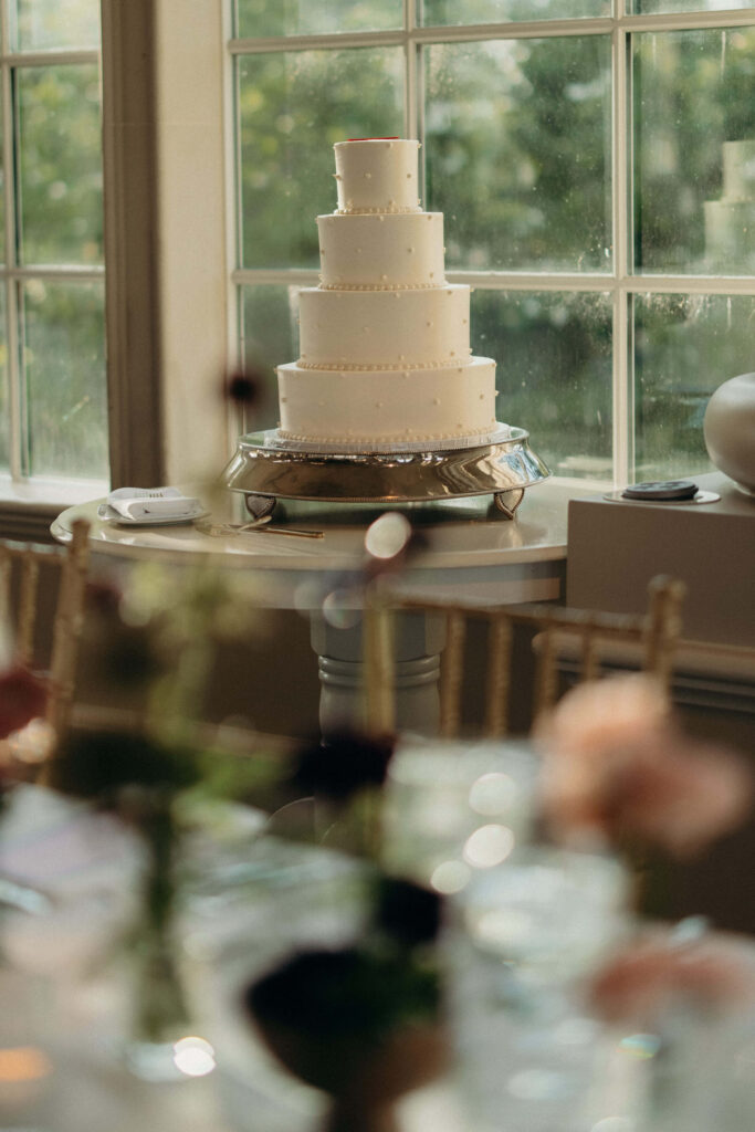 A four-tier white wedding cake displayed on a table at The Ashford Estate
