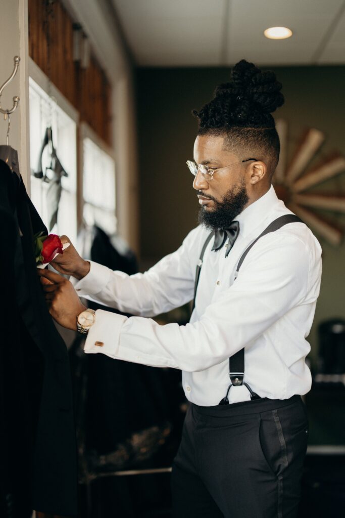 Groom adjusting the red rose boutonniere on his tuxedo jacket at Perona Farms