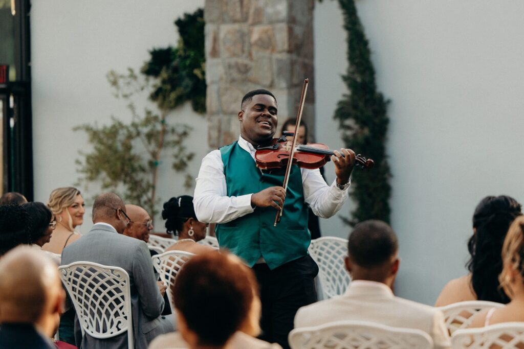 Violinist in a green vest playing live music for seated guests at Perona Farms