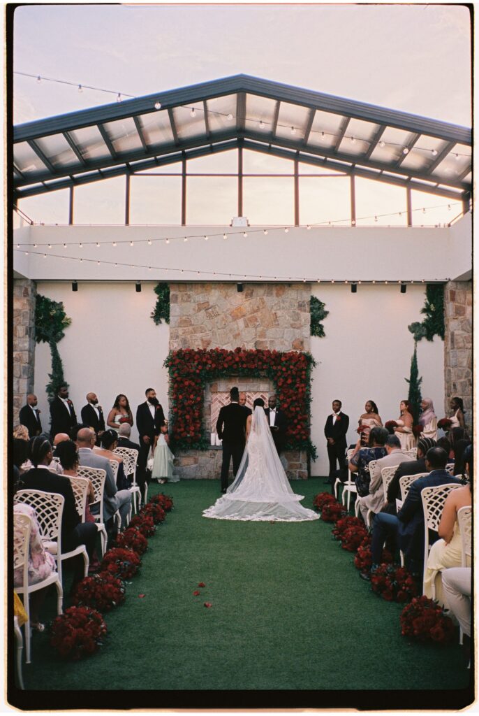 Wide shot of a wedding ceremony inside a glass-roofed atrium filled with guests at Perona Farms