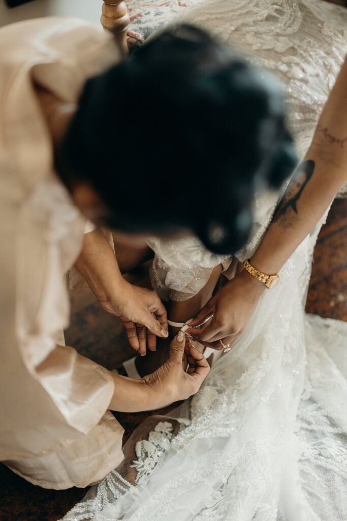 Close-up of hands fastening a garter onto the bride's leg at Perona Farms