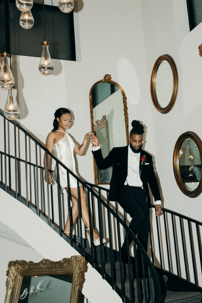 Bride in a short white dress and groom in a tuxedo walking down a staircase at Perona Farms