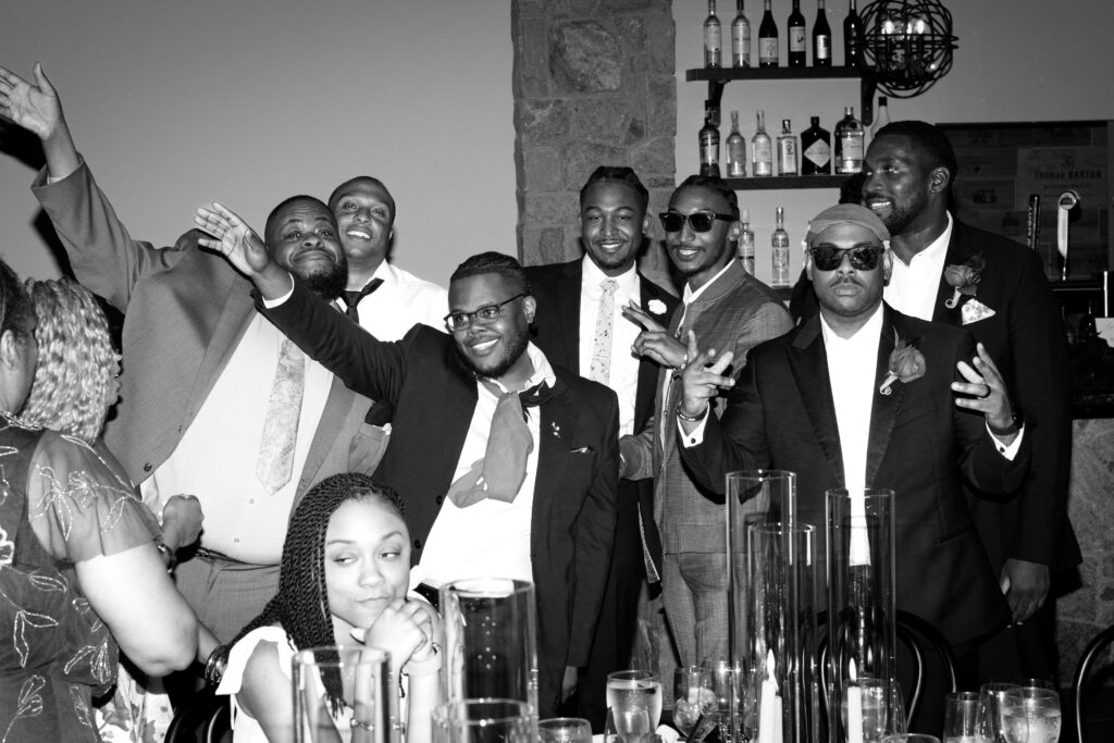 Black and white photo of wedding guests posing and celebrating at the bar inside Perona Farms