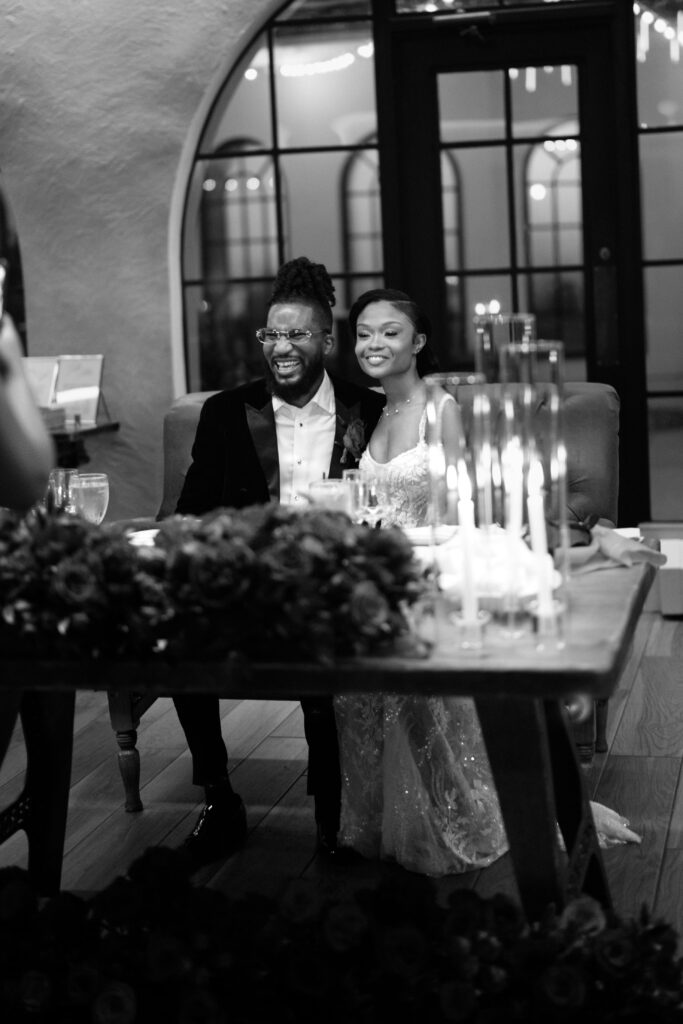 Black and white shot of the bride and groom smiling at their sweetheart table at Perona Farms