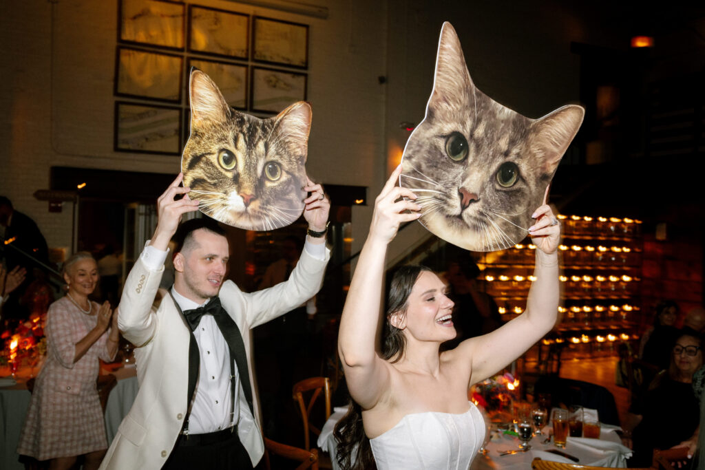Bride and groom holding up large cat cutout signs during their reception entrance at Battello