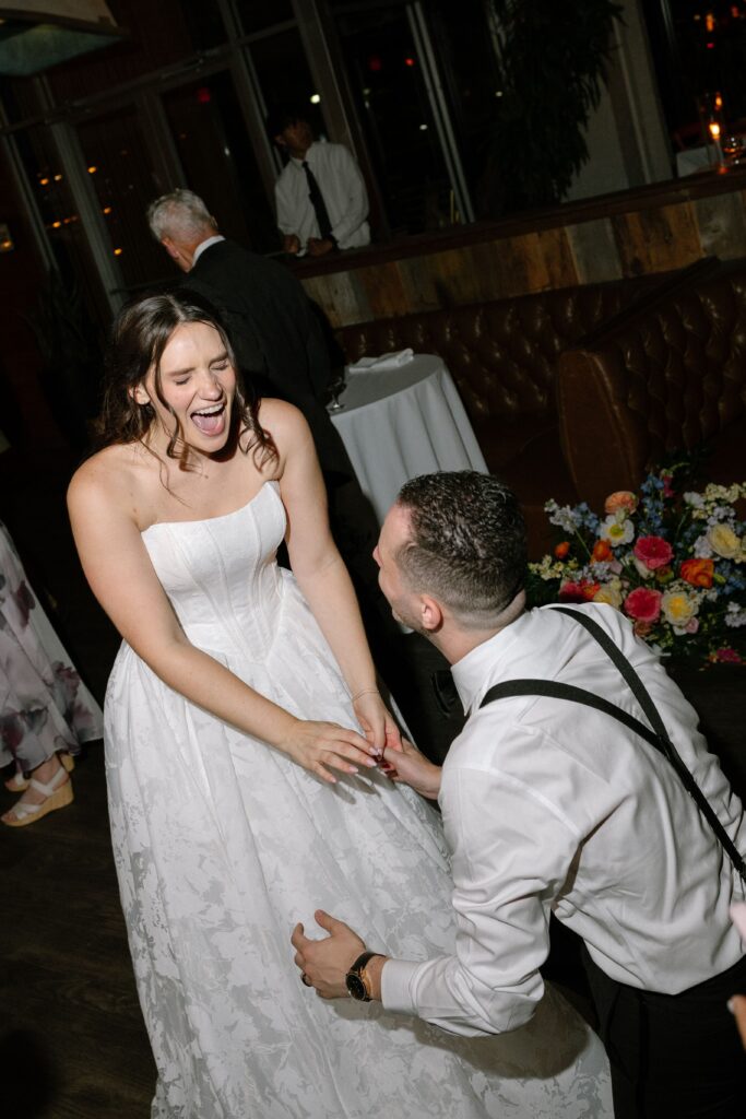 Groom kneeling and laughing while dancing with the bride at Battello