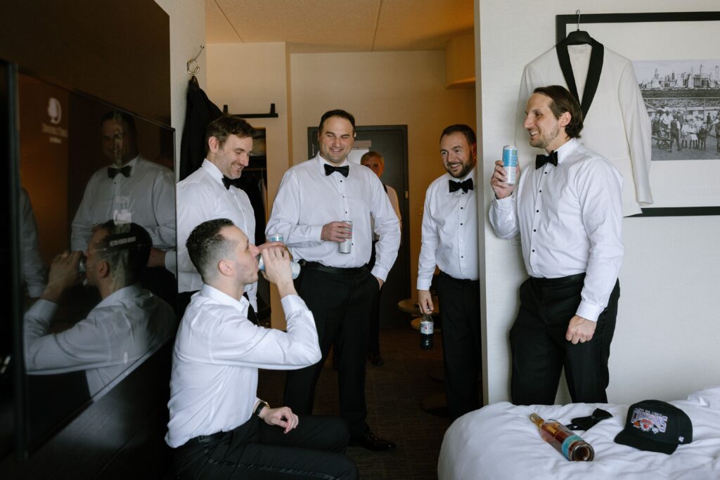 Groom and groomsmen drinking and celebrating in a suite before a wedding at Battello