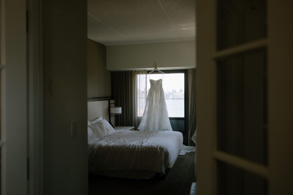 Wedding dress hanging in front of a window in a bridal suite before a ceremony at Battello