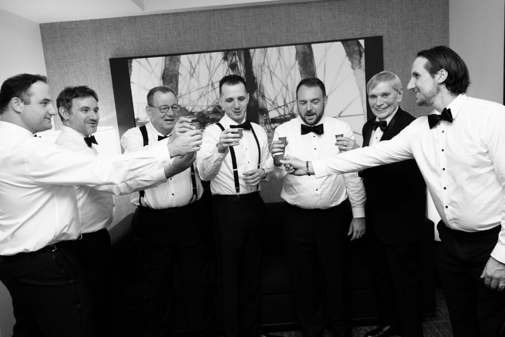 Black and white photo of the groom and groomsmen raising a toast together before a wedding at Battello