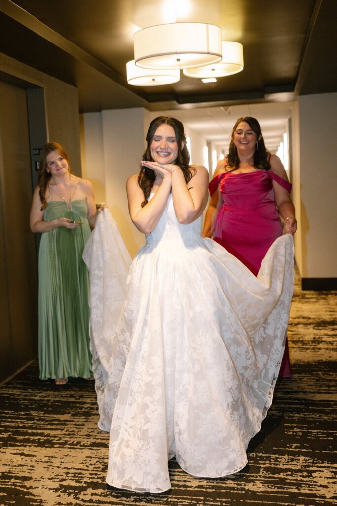 Bride happily walking down a hotel hallway with her bridesmaids holding her wedding dress train at Battello