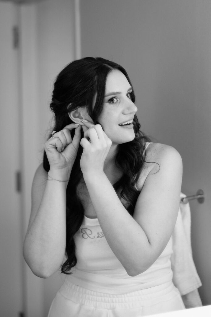Black and white photo of a bride putting on earrings while getting ready for a wedding at Battello