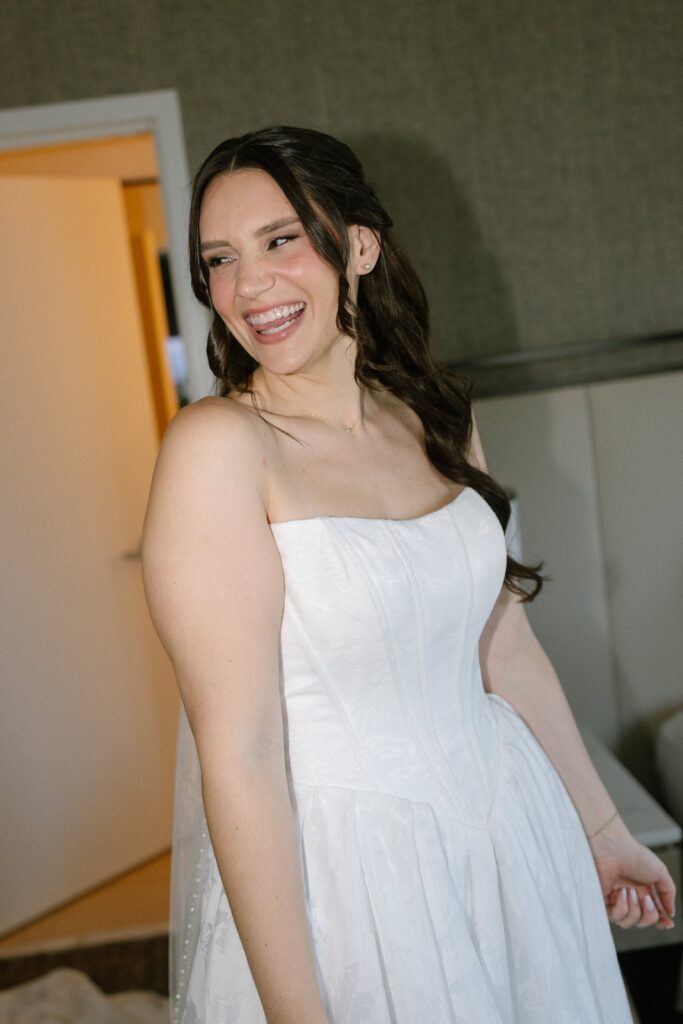 Smiling bride wearing a white strapless gown in a bridal suite before a wedding at Battello