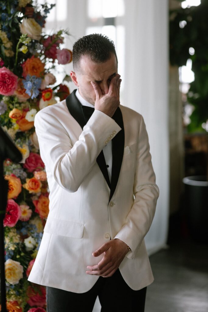 Groom in a white tuxedo jacket wiping away tears at Battello