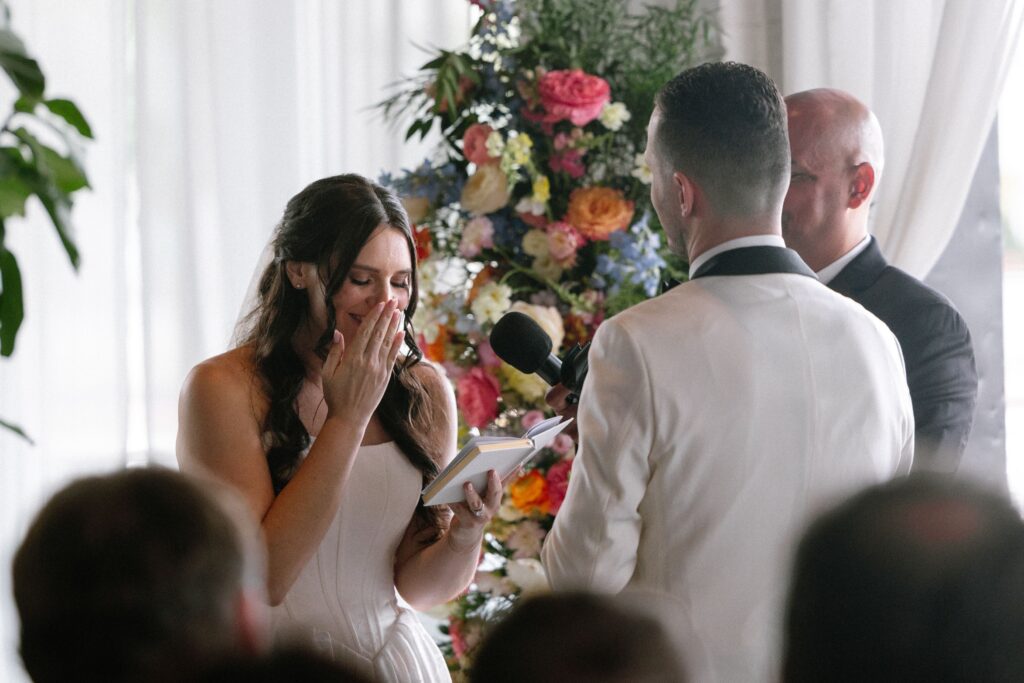 Bride laughing behind her hands while reading vows at Battello