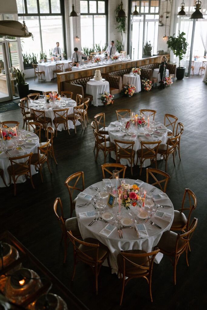 Wedding reception venue setup with decorated round tables and dark wood flooring at Battello