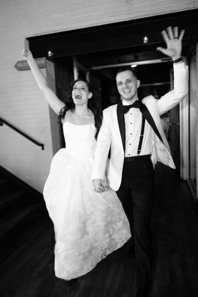 Black and white image of a happy newlywed couple making their grand entrance at Battello