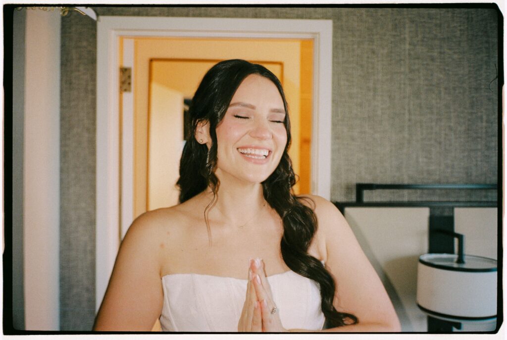 Close-up portrait of the bride smiling with her hands pressed together while getting ready for the wedding at Battello