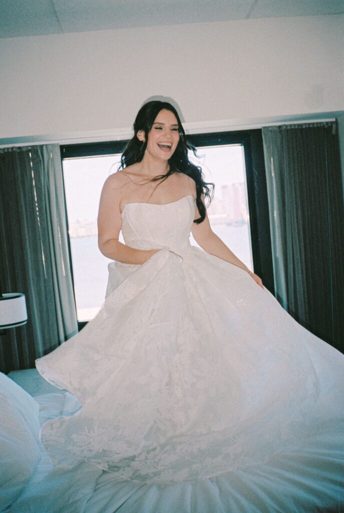 Bride laughing and spinning in her wedding dress on a bed before the ceremony at Battello